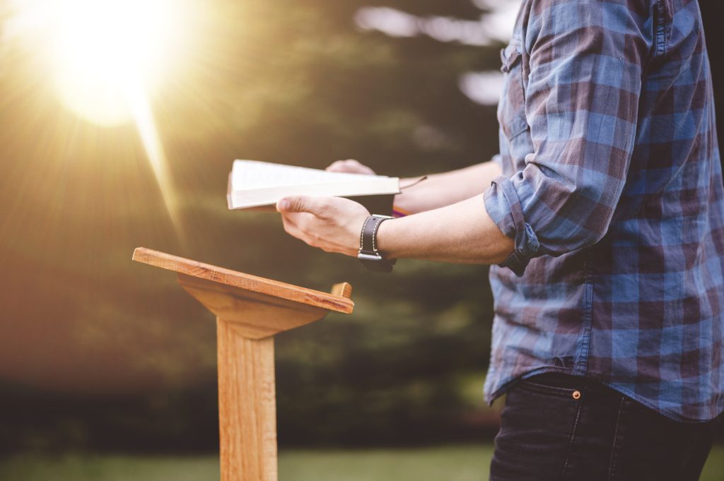 shallow-focus-shot-male-reading-bible-while-standing-near-podium